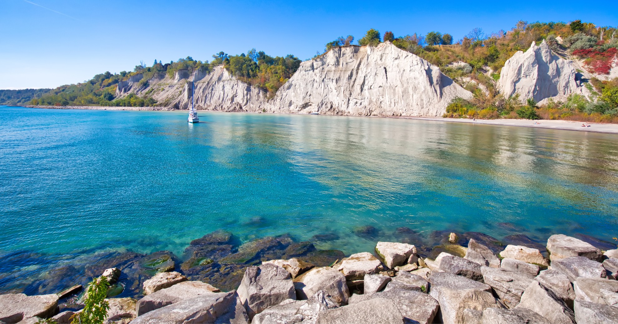 Lakeside with blue water, and the shore lined with rocks.